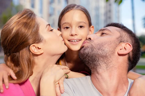 Vrolijke liefhebbende ouders hun jonge dochter kussen — Stockfoto