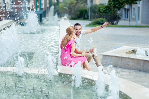 Trevligt ungt par tar selfies nära fontänen — Stockfoto