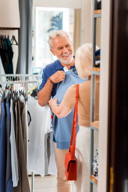 Mükemmel kumaş. Yüksek kalitesi hakkında övünme ederken eşimavi pullover gösteren duygusal gri saçlı müşteri