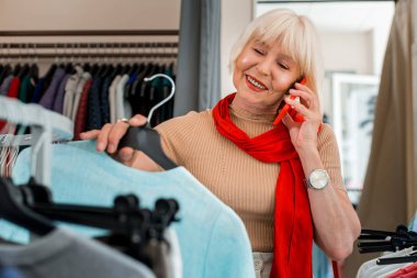 Tavsiye istiyorum. Cep telefonu üzerinden arkadaşı ile konuşurken ve alışveriş hakkında ona danışmanlık yaparken elbise ile bir askı tutan sevimli yaşlı kadın Bel kadar