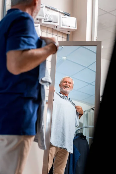 Emotional Grey haired man välja en T-shirt framför shopping spegel — Stockfoto