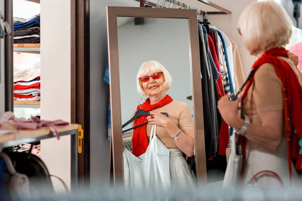Moderne grijs haired vrouw op zoek in kledingwinkel spiegel — Stockfoto