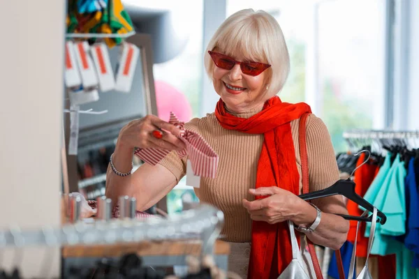 Blij grijs haired vrouw het kiezen van een hoofdband in winkel Winkel — Stockfoto