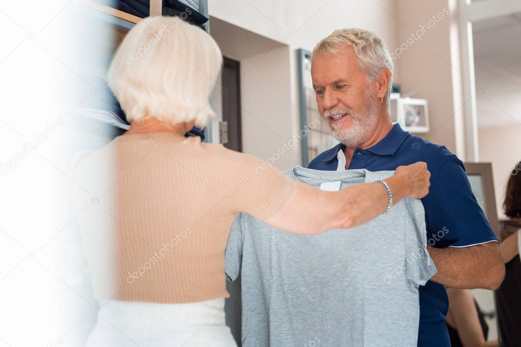 Positive husband accepting chosen T-shirt from his wife in shopping store