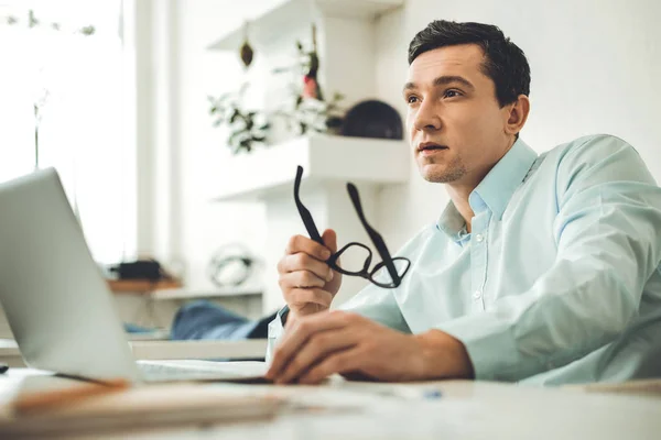 Netter nachdenklicher Mann, der zu Hause seine Brille hält — Stockfoto