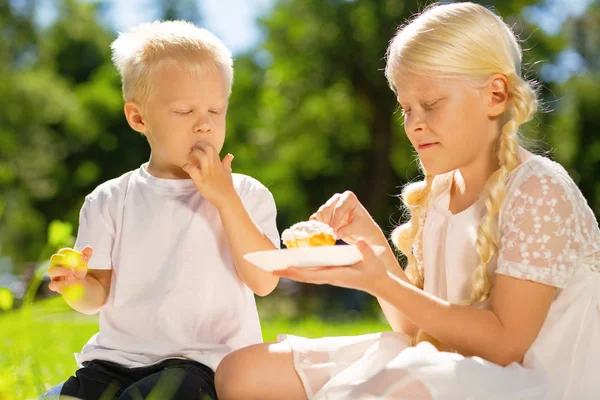 Happy brother and sister eating a cake in the park