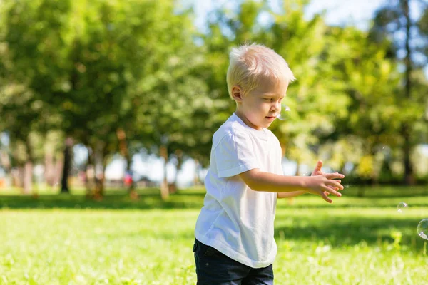 Cute schoolboy catching magic soap bubbles in the garden — Stock Photo, Image