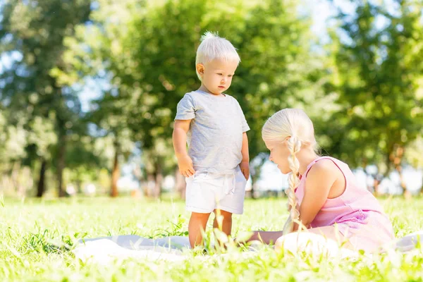 Příjemná sestra a bratr sedí na trávě v parku — Stock fotografie