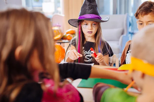 Dark-haired girl wearing black wizard hat for Halloween playing with friends