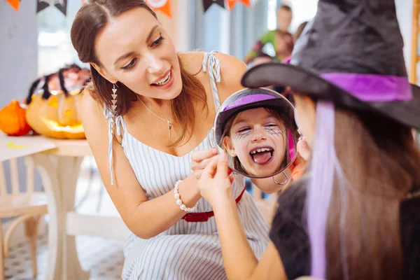 Kochająca matka trzyma lustro wyświetlone córka jej makijaż Halloween — Zdjęcie stockowe