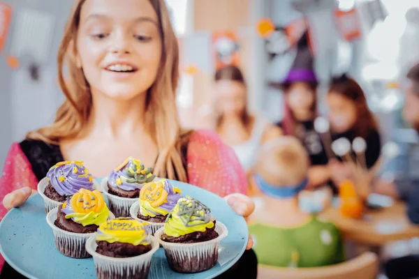 Beautiful blonde-haired girl feeling happy holding plate with celebration cupcakes