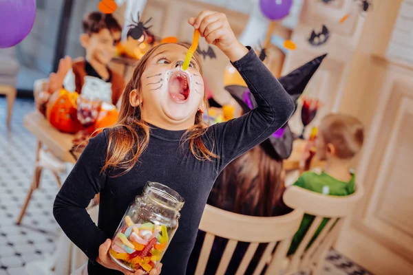 Funny girl feeling excited and overemotional eating gummy worm from the jar