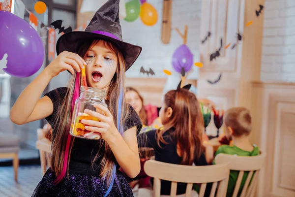 Dark-haired schoolgirl wearing wizard suit for Halloween party eating sweets