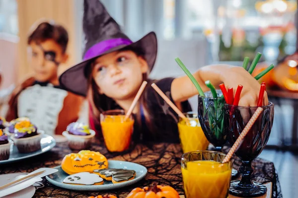 Girl wearing wizard hat for Halloween drinking juice and eating gummy sweets