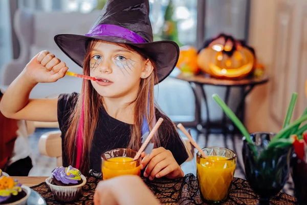 Cute girl wearing wizard Halloween suit enjoying thematic sweets and juice — Stock Photo, Image