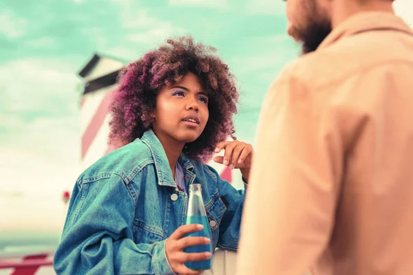 Chica joven curiosa sosteniendo la botella y escuchando atentamente a un hombre joven —  Fotos de Stock