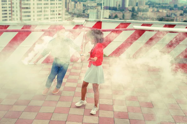 Two young people standing on the roof and being surrounded with white smoke
