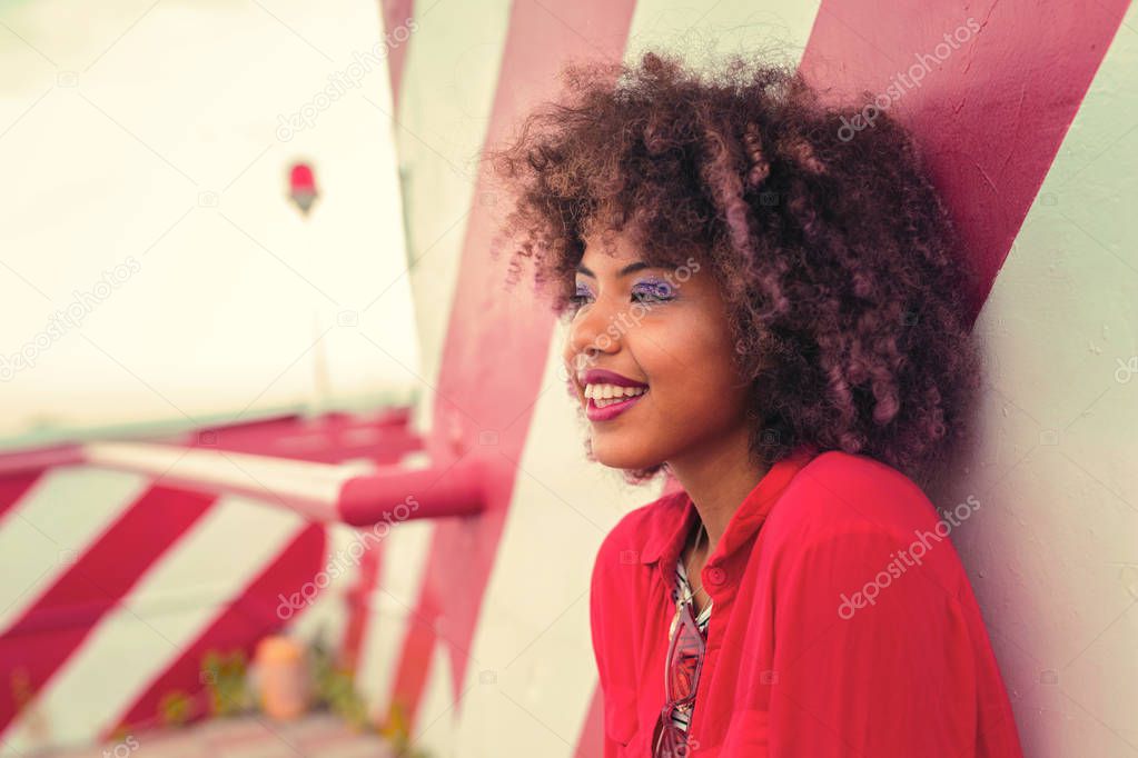 Portrait of beautiful curly girl leaning on the wall and smiling