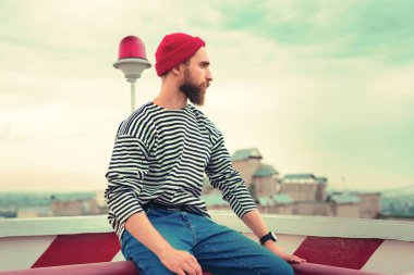 Şapkalı adam. Alışılmadık giysiler giyiyor ve düşünceli çatıdan mesafe içine bakarak sakin yakışıklı sakallı adam