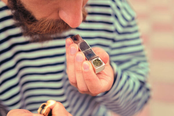 Bearded man holding lighter and tiny metal pipe before smoking