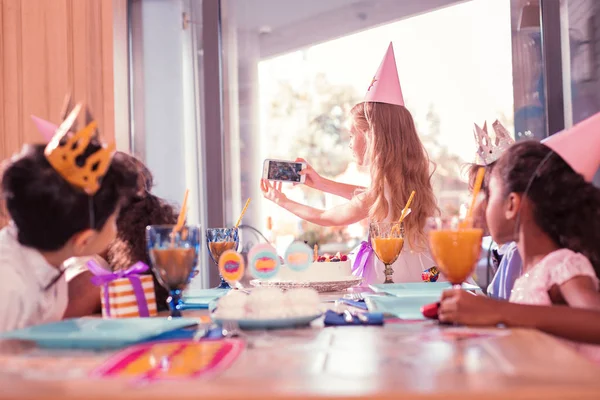 Careful birthday girl holding smartphone and taking selfies with friends — Stock Photo, Image