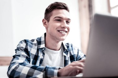 Happy young man smiling and looking at the screen of his laptop clipart