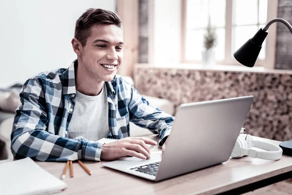 Homem alegre sorrindo e olhando para seu laptop moderno — Fotografia de Stock