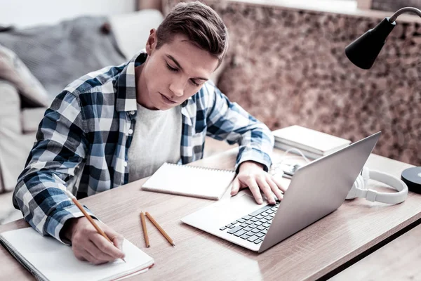 Étudiant attentif prenant des notes tout en faisant des devoirs — Photo