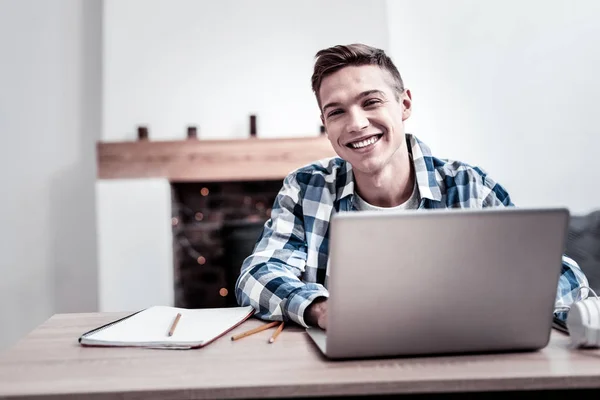 Menino alegre sorrindo enquanto sentado com laptop e se sentindo feliz — Fotografia de Stock