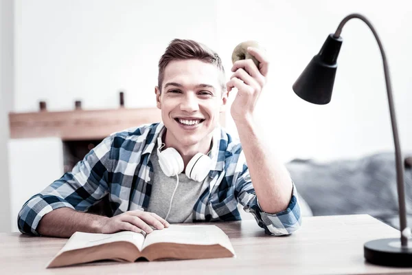 Positive student smiling while reading and holding apple — Stock Photo, Image