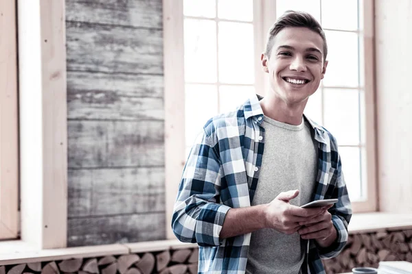 Aufgeregter junger Mann steht mit seinem Smartphone und lächelt glücklich — Stockfoto