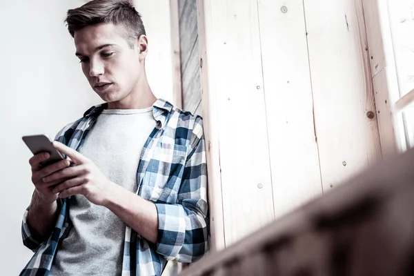 Hombre guapo con ropa casual y de pie junto a la ventana con su teléfono inteligente — Foto de Stock