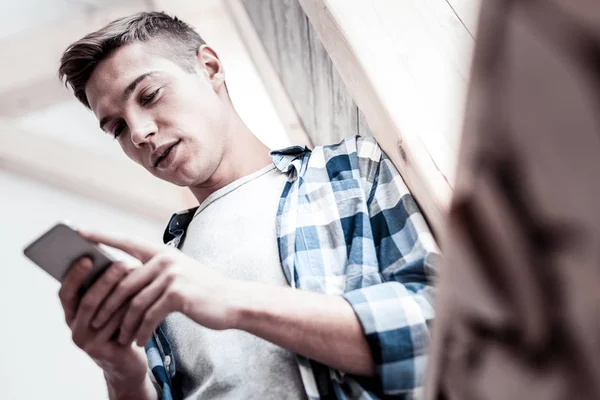 Tranquilo joven escribiendo mensajes mientras está de pie junto a la ventana — Foto de Stock