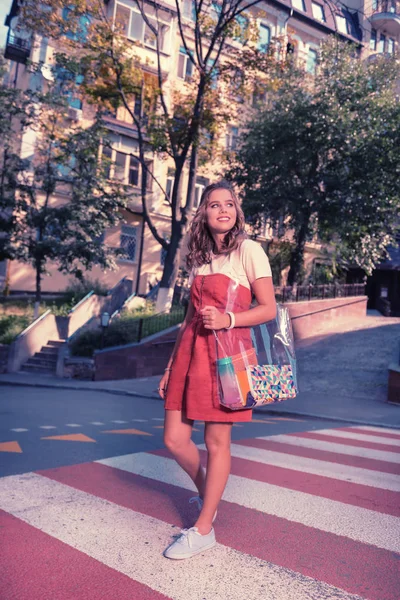 Сияющая темноволосая девушка в стильном красном платье, переходящем улицу — стоковое фото