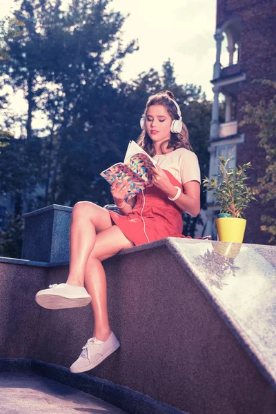 흰색 운동 화와 밖에 앉아 빨간 여름 드레스 입고 아름 다운 소녀 — 스톡 사진