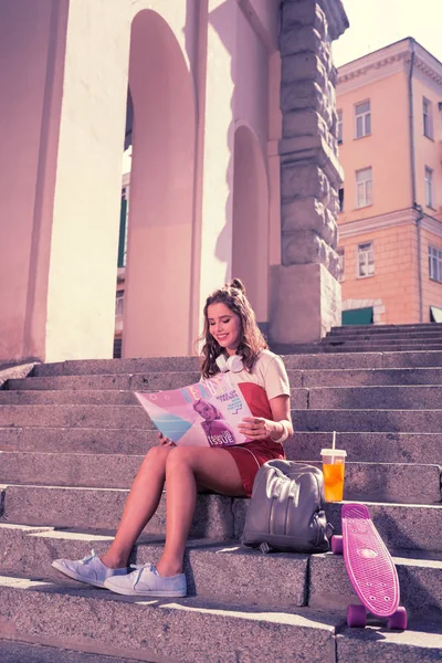 Strahlende junge Frau genießt ihr Wochenende mit Magazin und Sommercocktail — Stockfoto