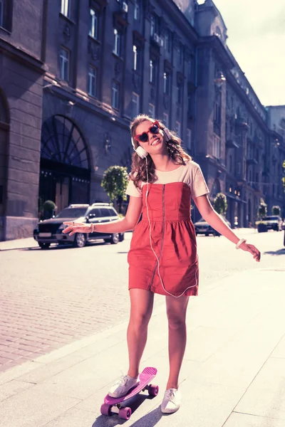 Extrem glückliches Mädchen in stylischer Kleidung und Accessoires auf Skateboard stehend — Stockfoto