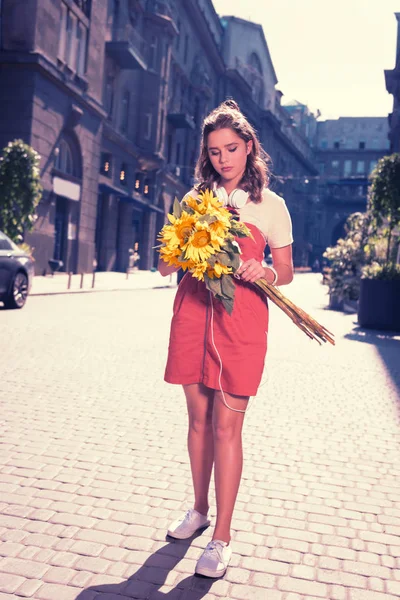 Curly dark-haired woman walking home with beautiful bright sunflowers — Stock Photo, Image