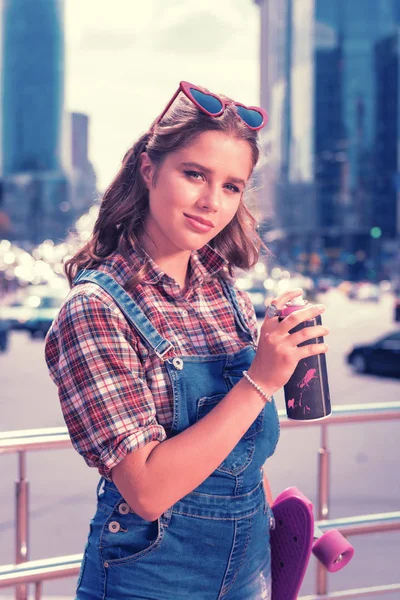 Modern street style girl holding energy drink and her purple skateboard