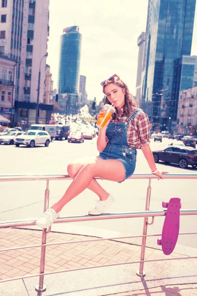 Chica moderna aficionado al skateboarding tener un poco de descanso mientras bebe bebida fría —  Fotos de Stock