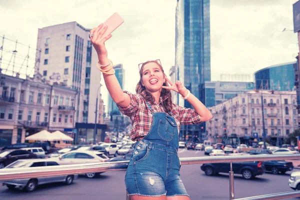Joven chica de moda mostrando señal de paz mientras hace selfie en su teléfono — Foto de Stock