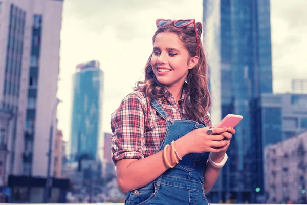 Lockigt student håller hennes rosa telefonen medan du skriver meddelandet hennes pojkvän — Stockfoto