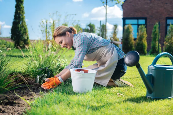 Good-looking woman leaning on her garden bed while planting new little flowers — Stock Photo, Image