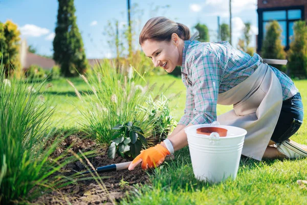 Beaming gardener holding little hoe in her hands while grubbing weeds up — Stock Photo, Image