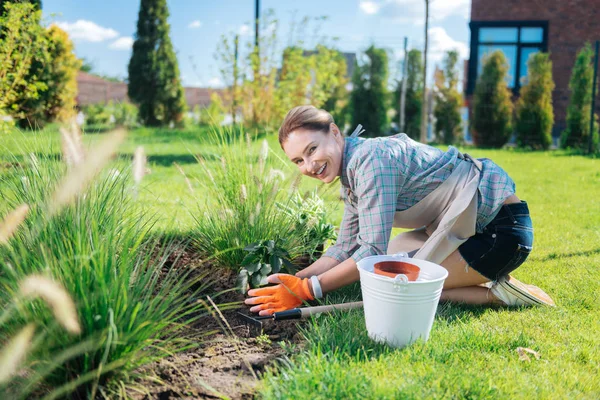 Blonde-haired smiling gardener wearing short denim shorts and white sneakers — Stock Photo, Image