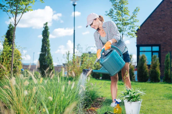 Светловолосая женщина в пиковой кепке поливает свое садовое ложе — стоковое фото