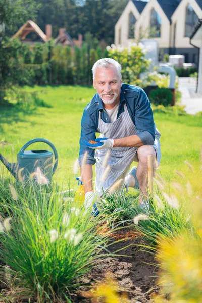 Bonito marido sorrindo enquanto se sente feliz ajudando sua esposa no jardim — Fotografia de Stock