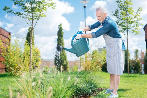 Grey-haired man wearing white gloves using garden sprinkler on hot summer day — Stock Photo, Image