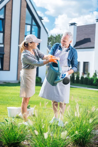 Žena nosí oranžové rukavice ukazuje její manžel způsob zalévání rostlin — Stock fotografie