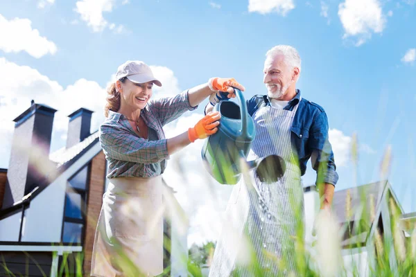 Mujer sonriente con gorra en pico que se une a su marido regando plantas —  Fotos de Stock